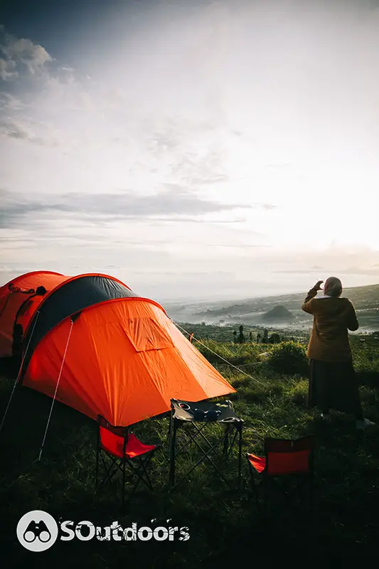Asian hijab woman camping with sunrise view in mountain near her orange tent
