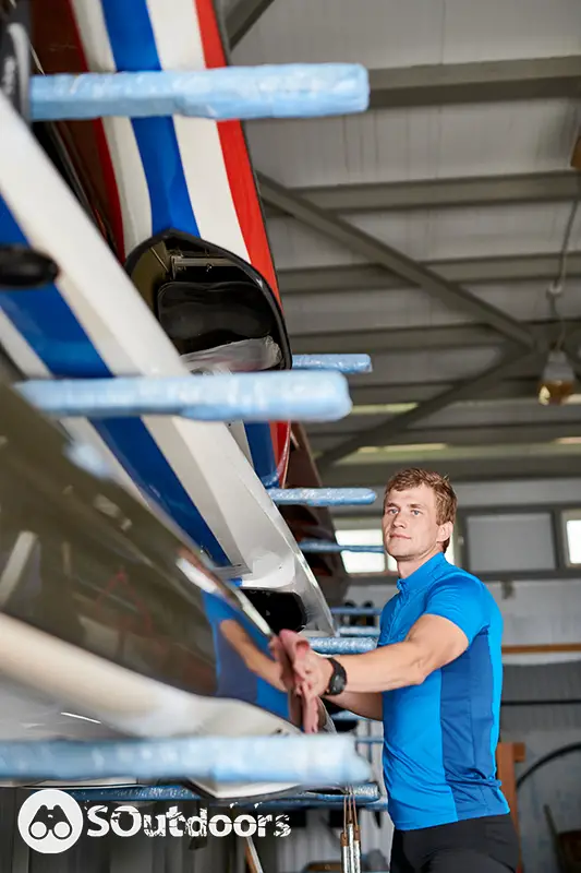 Young male athlete in sportswear wiping his kayak before competition in a warehouse