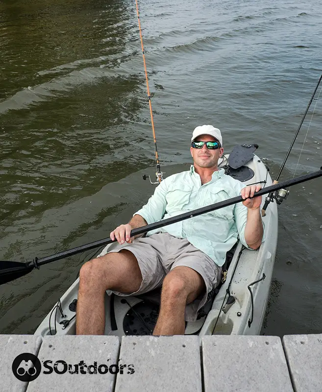 Man kicking back in fishing kayak while holding the paddle rod