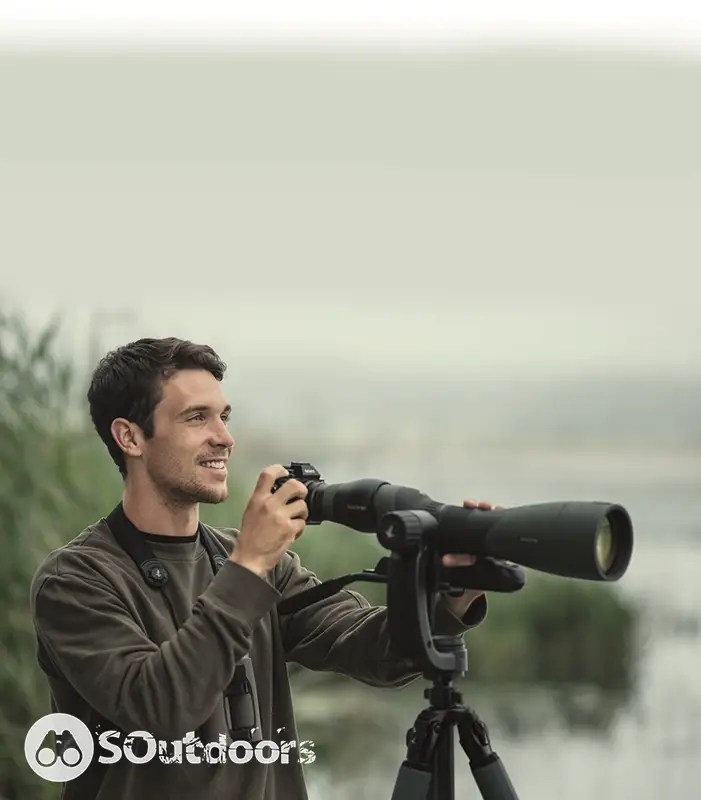 A man happily takes photographs using his camera attached to a spotting scope