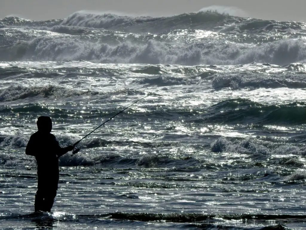 A man fishing be the seashore with big waves on the background